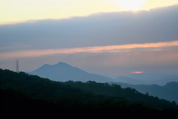 Stunning sunrise over Wuzhishan Mountain in Xizhi, New Taipei City, with soft orange and pink hues illuminating the misty hills and power line silhouette.