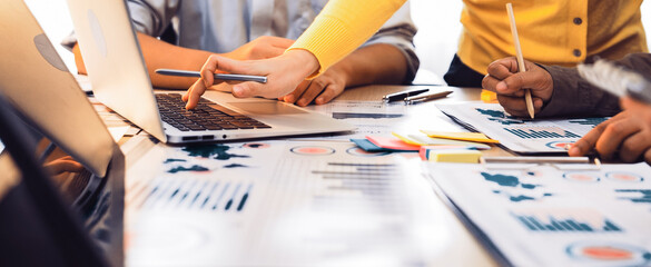 A dynamic team collaborates around a table filled with laptops, charts, and documents, focusing on data analysis and strategic planning for future business success. SACTR