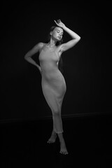 Black and white low key portrait of slender young barefoot woman in dress full length
