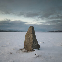 Single Rock in Snowy Barren Plain Under Overcast Sky