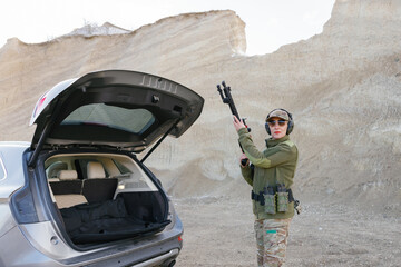 Female Soldier Holding Shotgun near Car with Open Trunk in Desert Area © nazariykarkhut