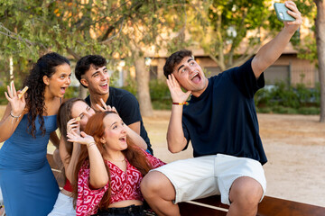 Group of cheerful students taking a selfie while eating snacks in a park
