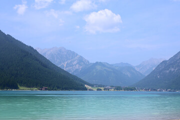 Obraz premium Beautiful view of Achensee lake with crystal clear turquoise water, forest-covered mountains, soft clouds in sky. Shot in Tyrol, Austria, scenic summer landscape captures calm, natural charm of Alps