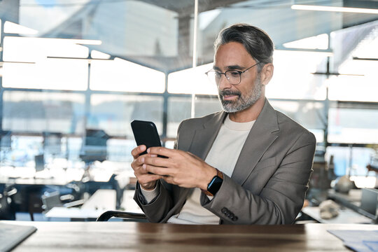 Busy mature business man investor thinking looking at mobile cell phone in office. Serious middle aged businessman executive using smartphone analyzing financial investment risks.