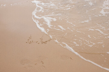 the wave washes away the inscription love on the sand