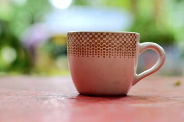 Ceramic tea cup with geometric patterns placed on a weathered table, capturing a quiet morning moment with a soft green bokeh background and natural light.