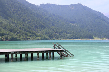 Wooden pier on the crystal-clear waters of Lake Achensee in Tyrol, Austria, surrounded by alpine mountains and moody summer skies. Peaceful travel destination in the Alps.