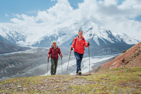 Smiling backpackers couple with backpacks and trekking poles during Lenin peak ascent with mountain peaks in background. Extreme active people, high-altitude Pamir area mountaineering concept - Powered by Adobe
