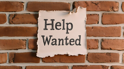 A weathered "Help Wanted" sign is posted on an aged brick wall, hinting at job opportunities in a quaint, vintage setting. Paper shows its wear and tear.