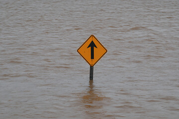 Flooded road sign with up arrow. High water levels submerge traffic infrastructure. Hazard warning in the midst of environmental event.