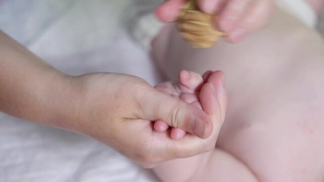 Slow-motion video of a ribbed juniper wood ball massaging an infant's right palm and fingers. Pediatric sensory stimulation therapy