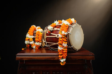 Traditional indian dholak drum decorated with orange and white flower garlands on a wooden table, studio lighting