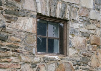 A small, square window, framed by weathered wood, is set within a thick stone wall.