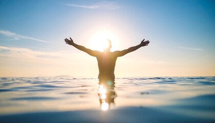 Fototapeta premium Silhouette of a man standing in the ocean with arms outstretched towards the sun