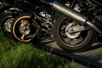 Obraz premium Motorcycle rear wheels with visible disc brakes and exhaust pipes parked on paved lot at outdoor gathering showcasing sportbike design, suspension, and modern braking technology
