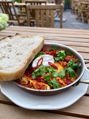 Shakshuka with Poached Egg, Yogurt and Fresh Bread on Wooden Table