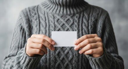 Person wearing a grey cable knit sweater holding a blank white business card