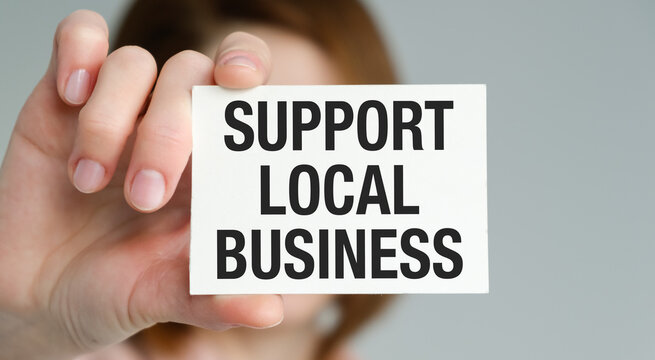 A person holding a white card that says Support Local Business