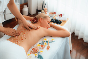 Fototapeta premium Woman customer having exfoliation treatment in luxury spa salon with warmth candle light ambient. Salt scrub beauty treatment in health spa body scrub. Quiescent
