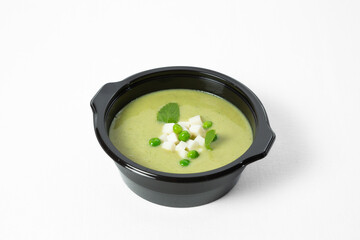 Cold green pea soup with cheese cubes and mint leaves in a bowl on a white background