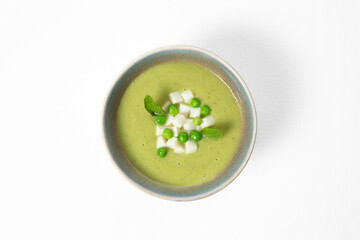 Cold green pea soup with cheese cubes and mint leaves in a bowl on a white background