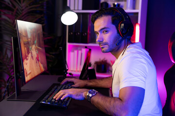 Smart gaming streamer enjoy playing battle team with streaming online shooting gun game with multi or single player at warship on pc screen, wearing headset at digital neon light cyber room. Surmise.