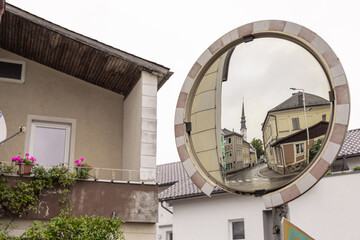 street scene in Bad Leonfelden, captured through a circular convex mirror. The mirror reflects a row of colorful buildings, a church steeple, and a wet street, suggesting recent rain. In the