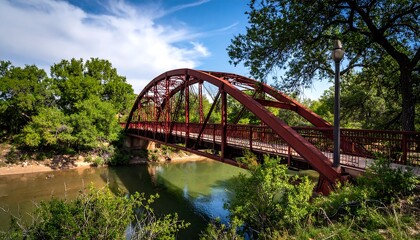 Naklejka premium Red Steel Arch Bridge Spanning a River, Framed by Lush Greenery and a Blue Sky