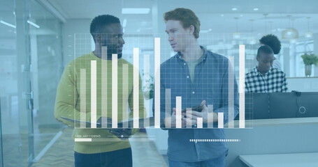 Walking two male coworkers holding tablet and gesturing in open-plan office corridor, chart overlay