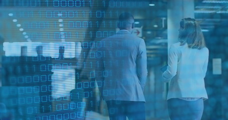Walking colleagues in blazers sharing cybersecurity data overlay in office corridor, holding tablet