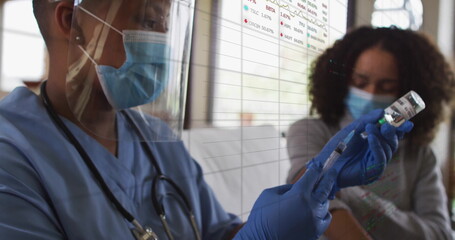 Medical professional wearing scrubs and gloves drawing vaccine from vial in clinic, with syringe