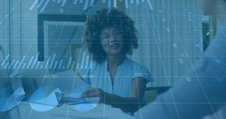 Discussing executive holding charts, speaking to colleague at office desk with monitor overlay