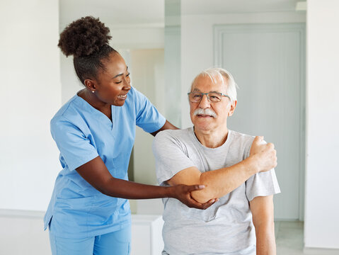 Doctor or nurse or physiotherapist caregiver exercise with senior man at clinic or nursing home