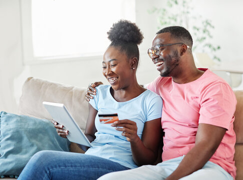 portrait of happy smiling young couple using a tablet computer and a credit card for online shopping at home, technology and internet use in everyday life concept - Powered by Adobe