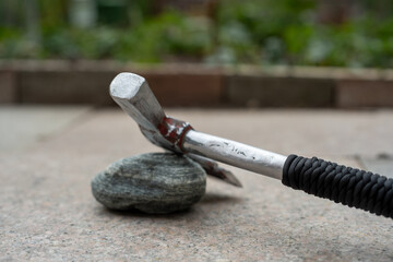 Modern Tactical Hatchet Resting on a Stone on a Concrete Ground