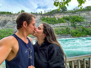 A young couple kiss while taking a selfie with the Niagara rapids and Escarpment in the background.
