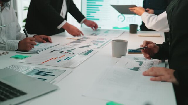 A diverse team of professionals engaging in a detailed business meeting, analyzing data charts and strategies while utilizing modern technology in a collaborative office environment. SACTR - Powered by Adobe