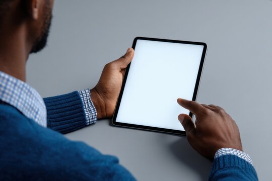 A close-up of an African American man's hands holding and interacting with his tablet, sitting at the table in front of him Generative AI