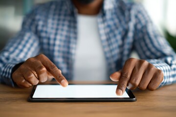 A close-up of an African American man's hands on his tablet, with the screen blank for mockup space He is wearing a blue and white checkered shirt sitting at a table in an office setting Generative AI