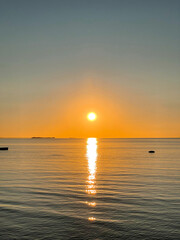 Beautiful sunset over the sea. The sun sets on the water. The sky is painted with bright colors. Sunset beach in summer evening. Vertical photography.
