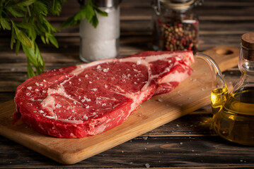Beef entrecôte on a cutting board next to an oil dispenser, salt, and pepper, with a rustic background. Close-up.