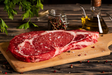 Beef sirloin steak on a cutting board with flaky salt, next to an oil dispenser and pepper, with a rustic background. Close-up.