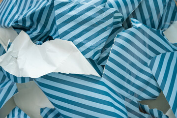 Close-up view of ripped blue and white striped wrapping paper after unboxing gifts. Minimalistic texture image reflecting unsustainable packaging habits and excess during holiday celebrations.