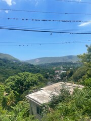 Hilltop view of a lush green valley with scattered houses and mountains in the distance under a clear blue sky.