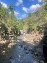Sunlit rocky creek flowing through a green valley under a bright blue sky — serene natural landscape perfect for outdoor and nature themes.