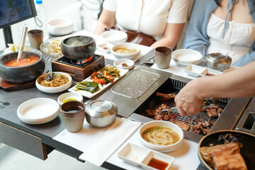 In a kalbi barbecue restaurant, a server grills a cut of meat over glowing coals, flames licking edges as steam rises from sizzling fat, filling the air with rich aroma. Seoul, Jung District, spring.