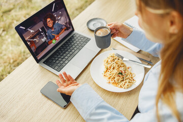 A person finds joy in savoring pasta and sipping coffee while participating in a virtual session on their laptop
