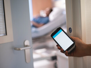 Hand holding smartphone in hospital setting with medical equipment showing healthcare technology adoption