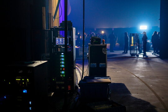 Professional audio visual production equipment and control systems in backstage area with blue lighting and crew