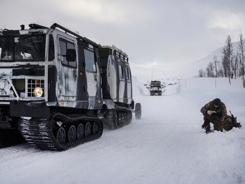 Tracked military vehicles with personnel in snowy arctic landscape during cold weather operation